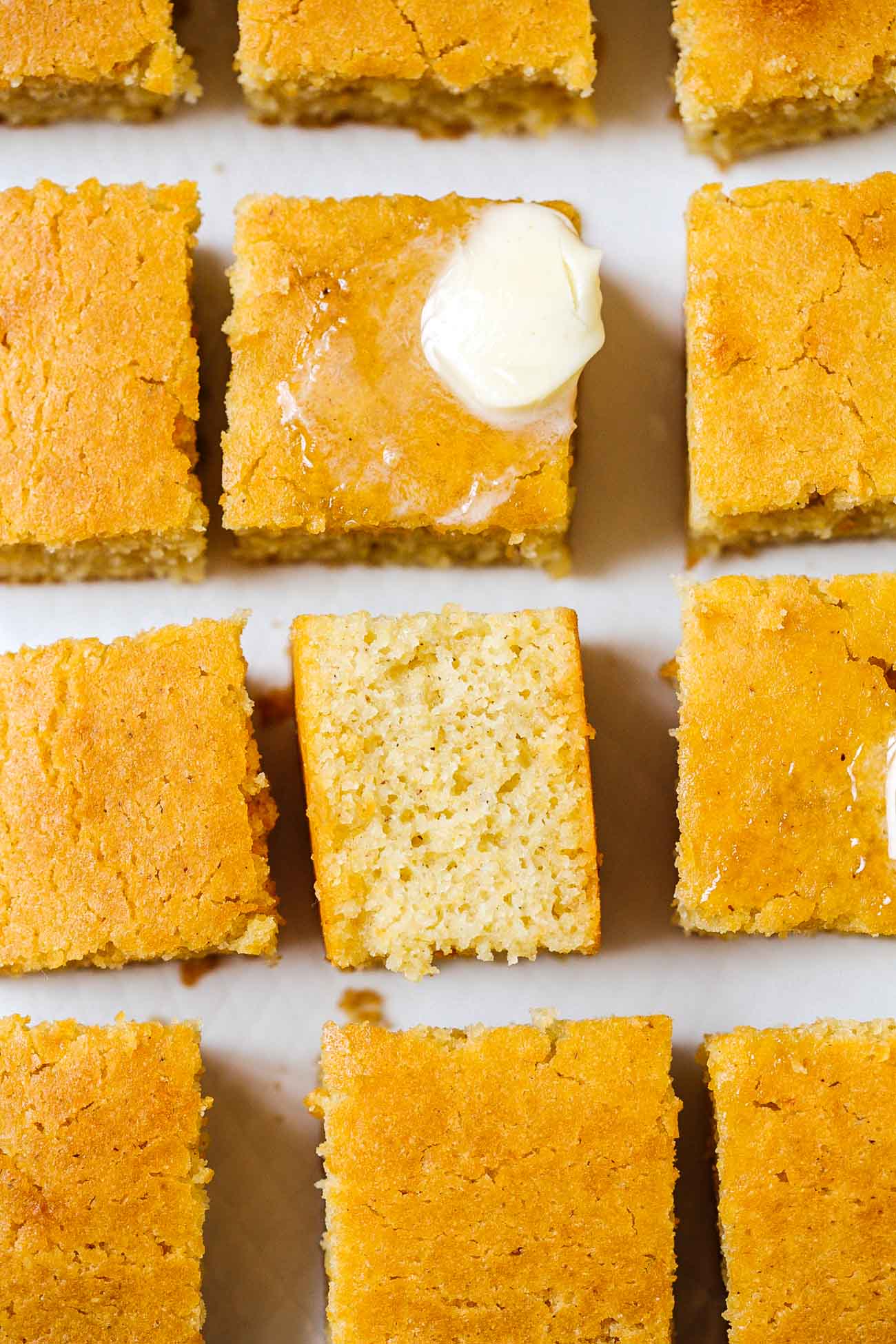 Pieces of gluten free cornbread, cut, with one flipped to show the texture of the inside and one with butter.