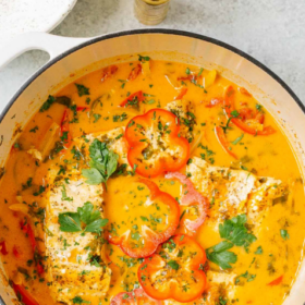 Overhead view of a pot filled with Brazilian Fish Stew (Moqueca) featuring fish fillets, tomato slices, herbs, and a creamy orange broth, all garnished with fresh parsley.