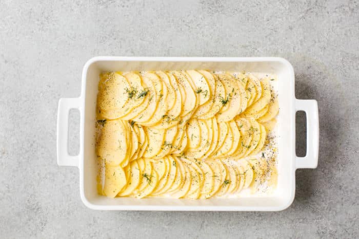 overhead view of white casserole containing sliced potato, milk and herbs