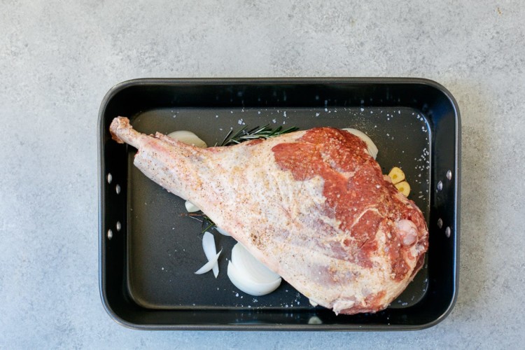 overhead view of raw leg of lamb on a roasting pan