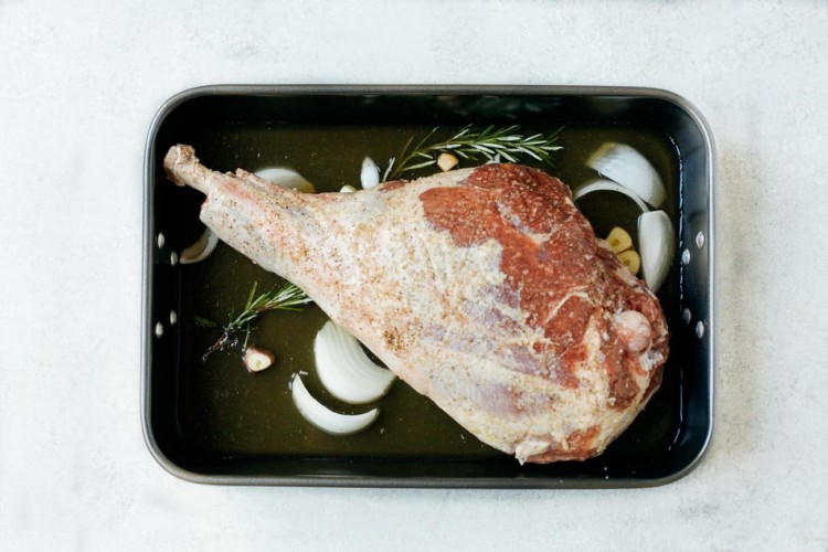 overhead view of raw leg of lamb on a roasting pan