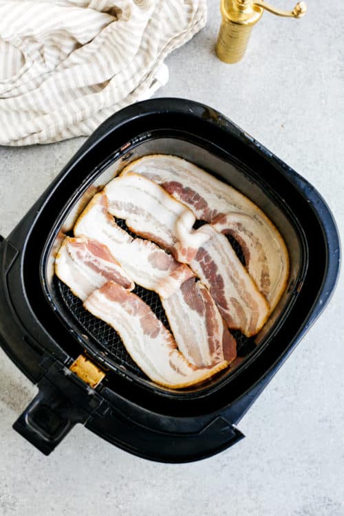 overhead view of raw bacon inside of a air fryer basket