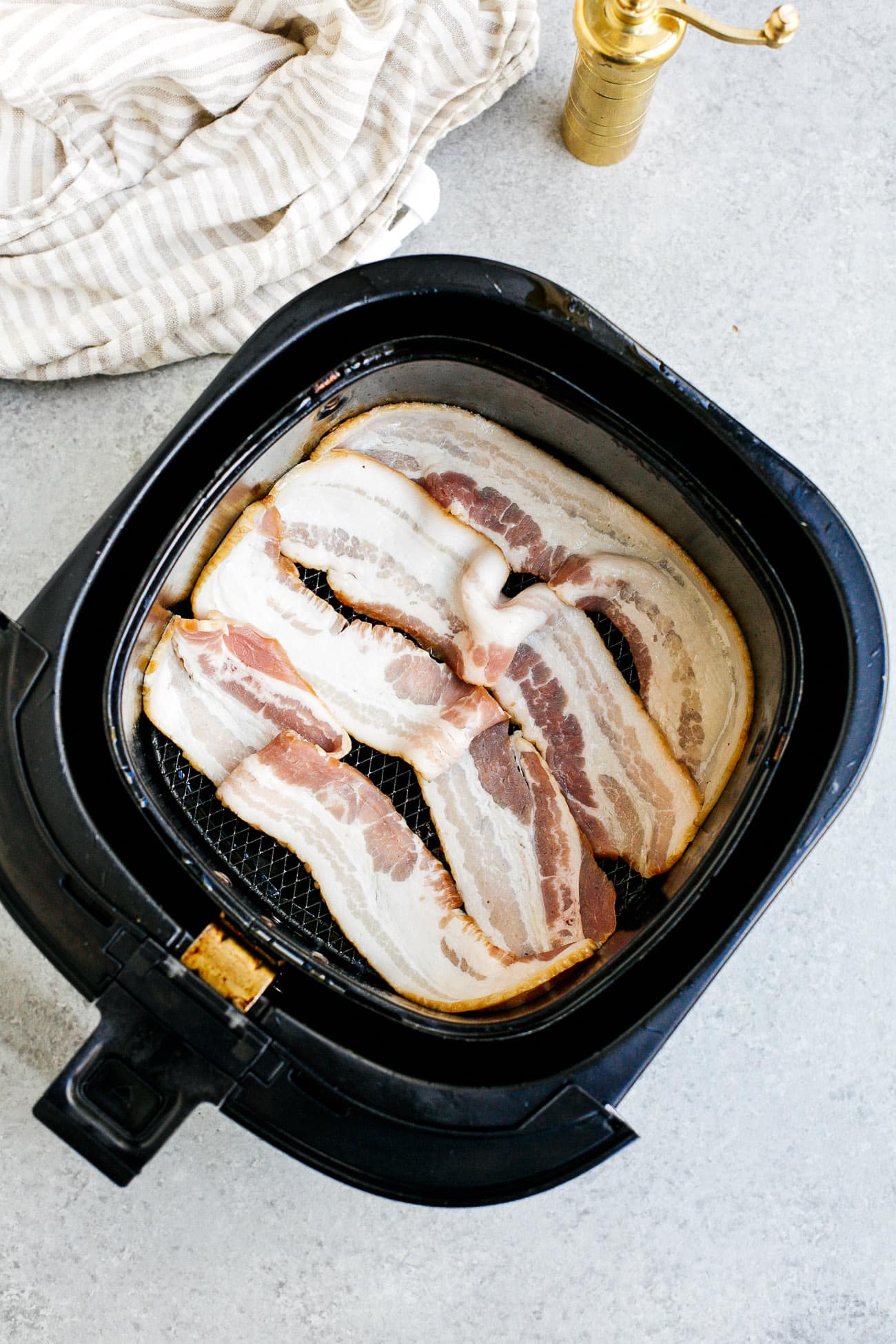 overhead view of raw bacon inside of a air fryer basket 
