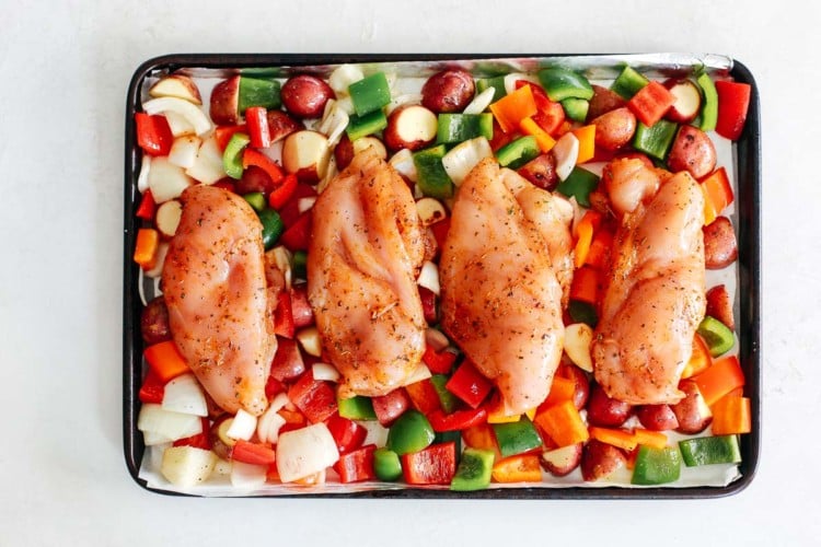 overhead view of vegetables and chicken breast on a baking sheet