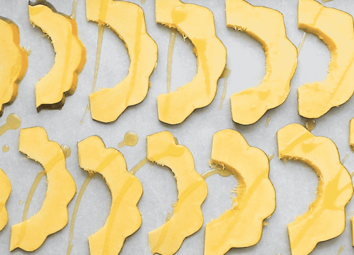 Sliced yellow squash pieces arranged on a baking sheet lined with parchment paper, drizzled with oil.
