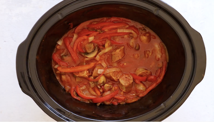 A Crockpot Sausage and Peppers dish with sausage, sliced red bell peppers, onions, and tomato sauce, all simmered together in a rich, red sauce.