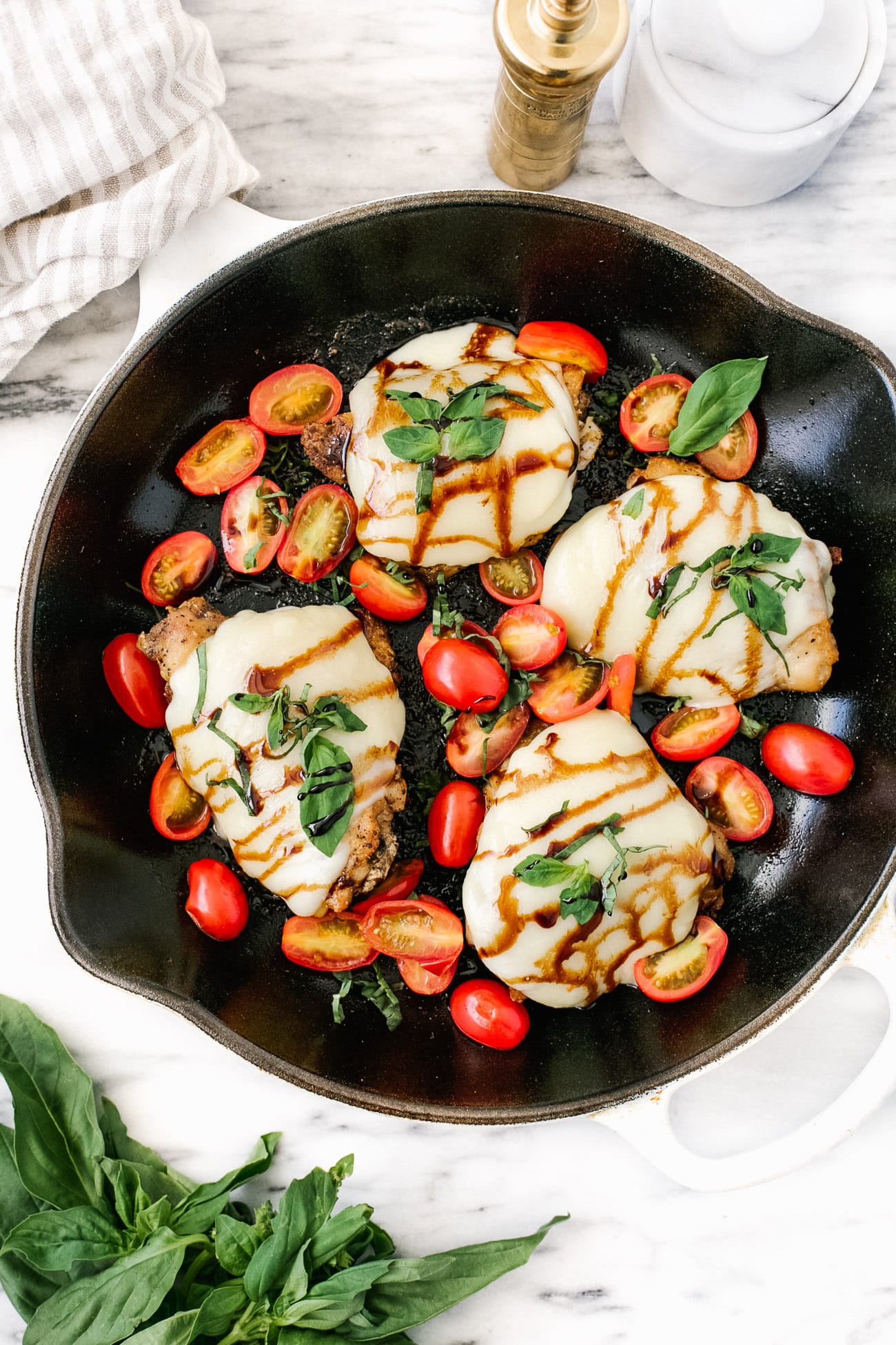 Overhead view of a skillet with baked caprese chicken thighs.