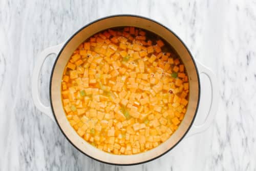 A large white pot on a marble surface filled with small diced orange vegetables, likely sweet potatoes, submerged in water—perfect for starting a hearty Sweet Potato Chicken Soup.