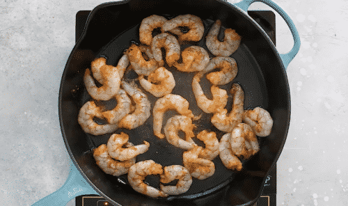 overhead view of a cast iron skillet with raw shrimp inside of it.