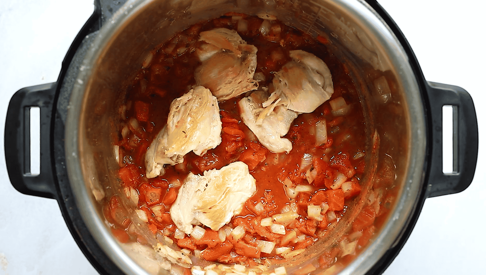 Overhead view of Instant Pot bowl containing chicken thighs and tomato sauce.
