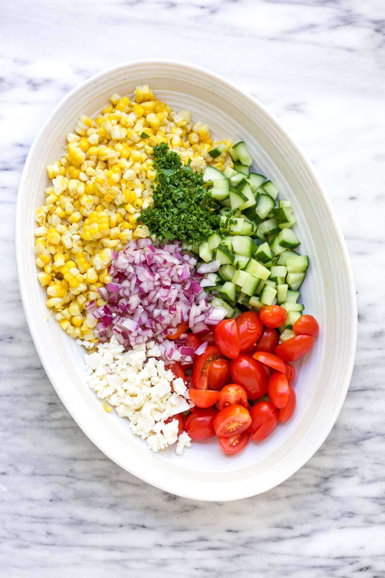 ingredients to make corn salad in a white bowl on a marble board