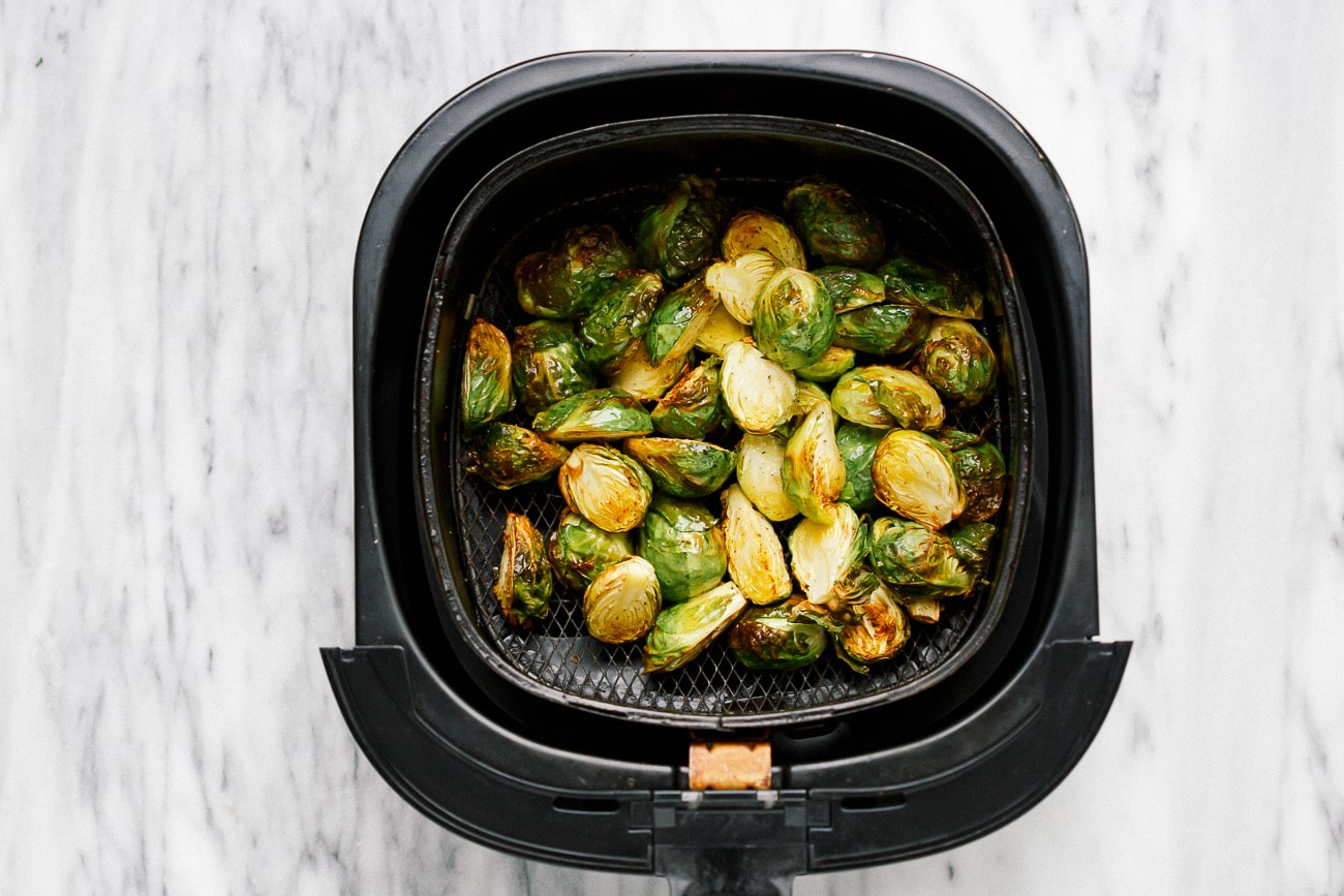 Cooked Brussels sprouts in a black air fryer basket.
