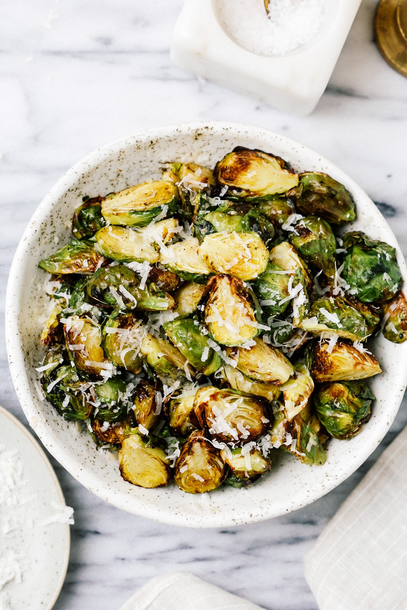 A serving bowl full of crispy Brussels sprouts topped with parmesan cheese. 