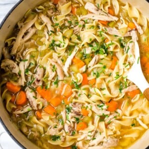 Chicken noodle soup in a large white pot.