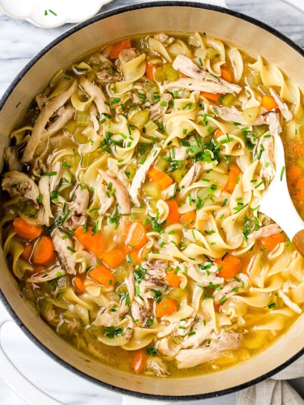 Chicken noodle soup in a large white pot.