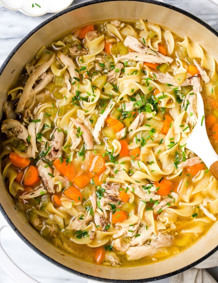 Chicken noodle soup in a large white pot.