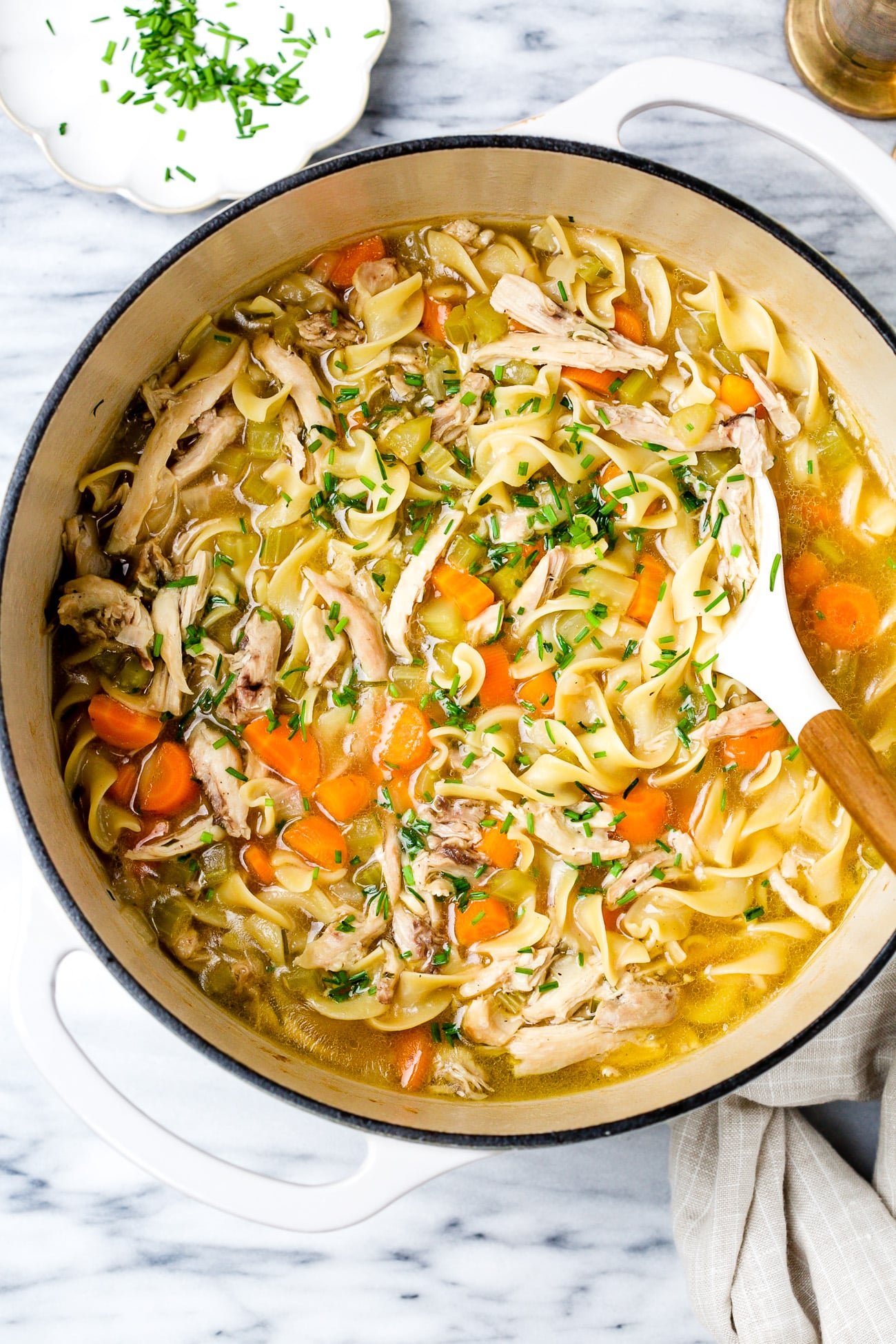 Chicken noodle soup in a large white pot.