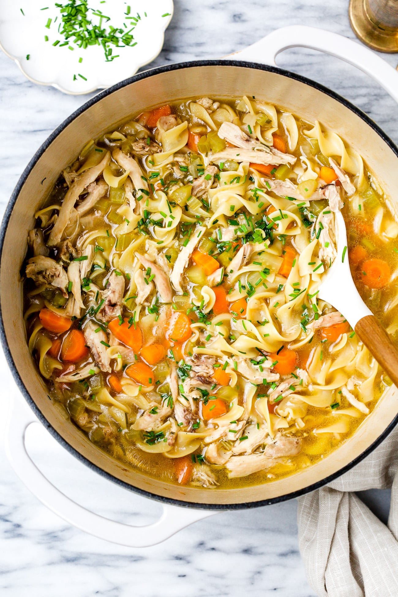 Chicken noodle soup in a large white pot.