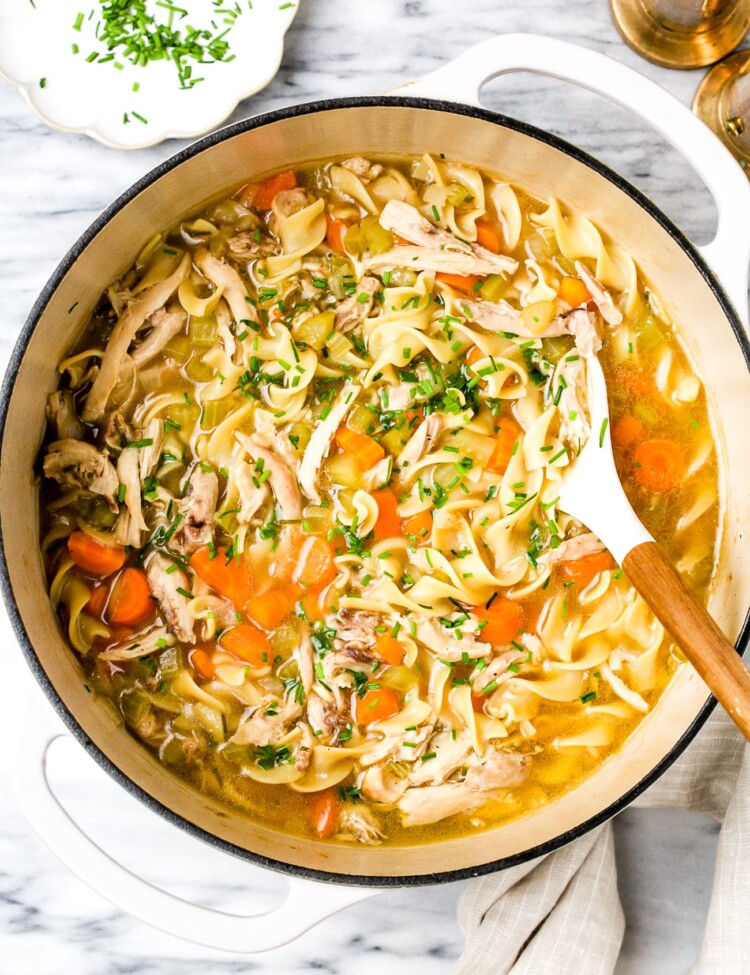 Chicken noodle soup in a large white pot.