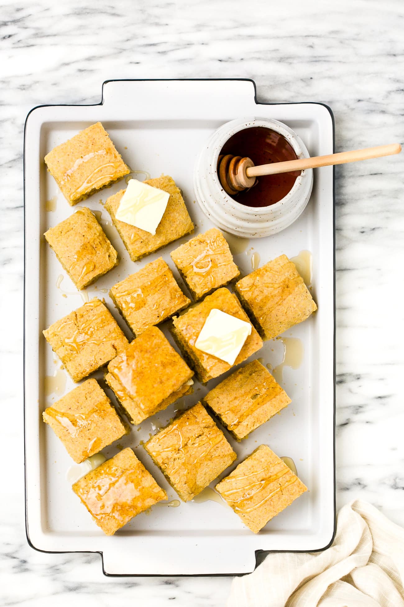 gluten-free cornbread on a white baking sheet with butter and honey on the top of the cornbread. 