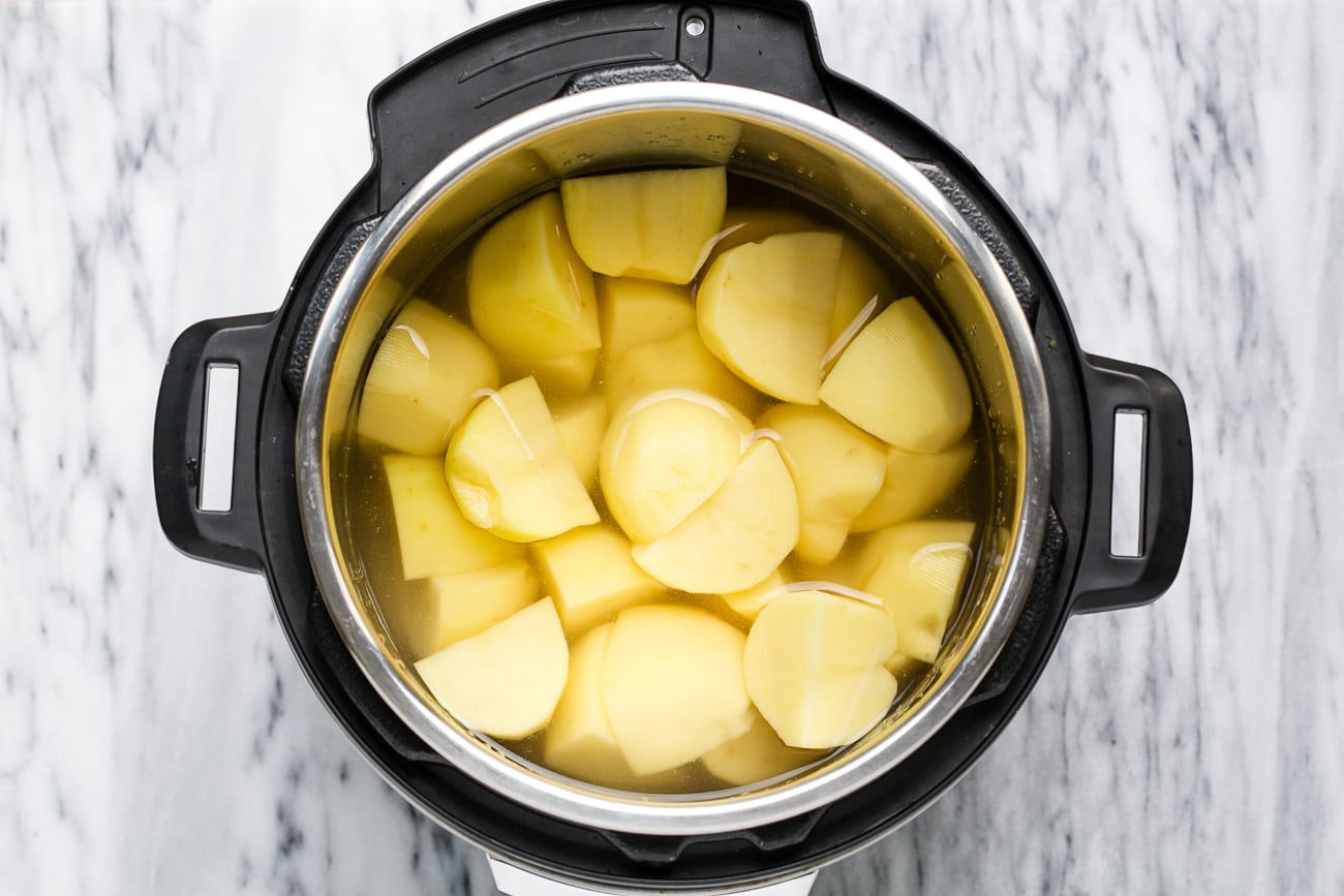 Peeled and quartered potatoes covered in water in an instant pot.