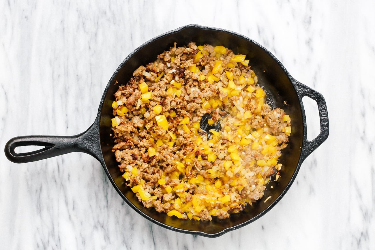 Onion, garlic and diced pepper added to browned meat in skillet.