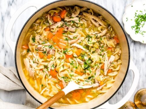 Chicken noodle soup in a large white pot.