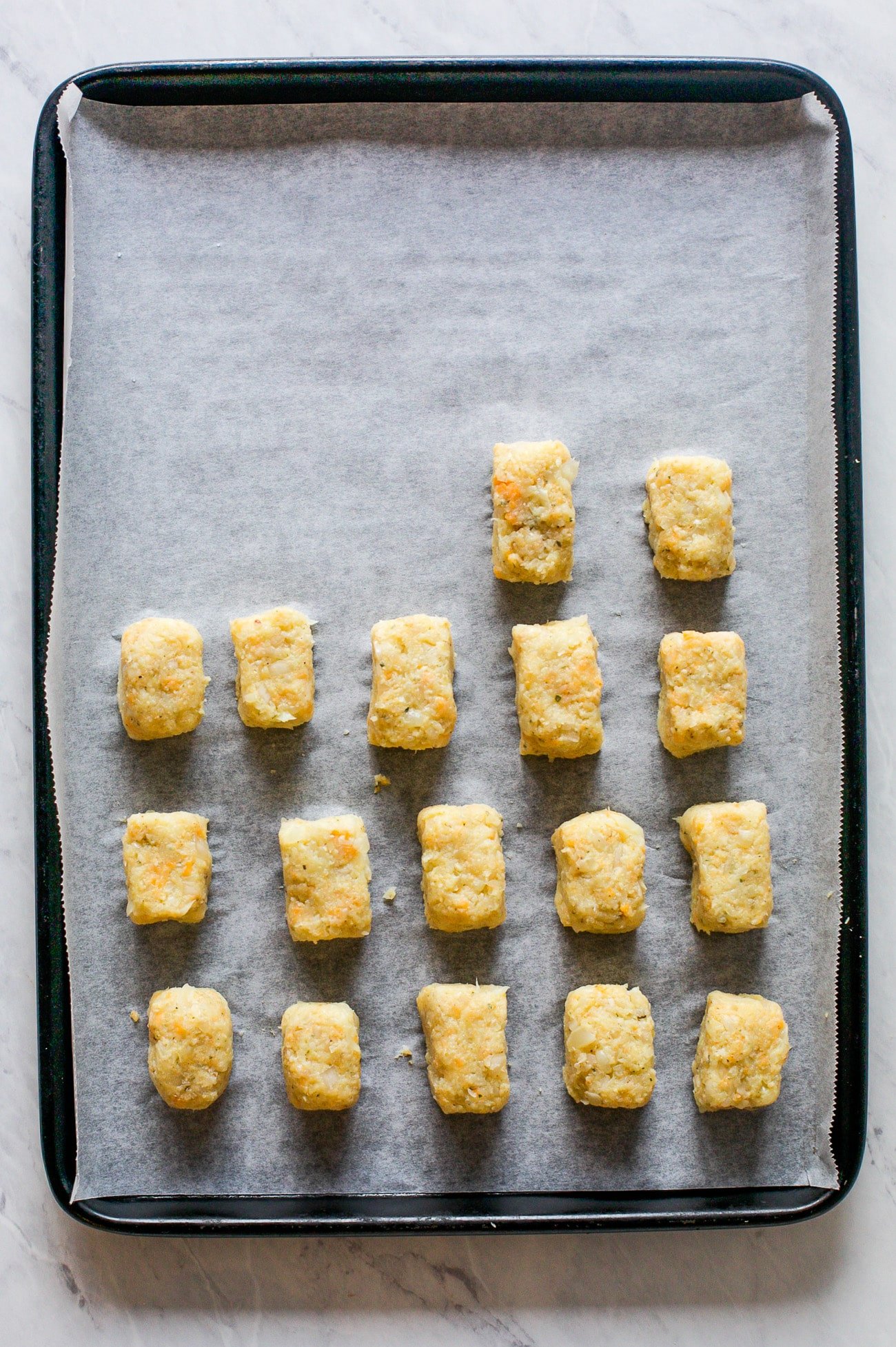 Unbaked tots on a parchment paper lined baking sheet.