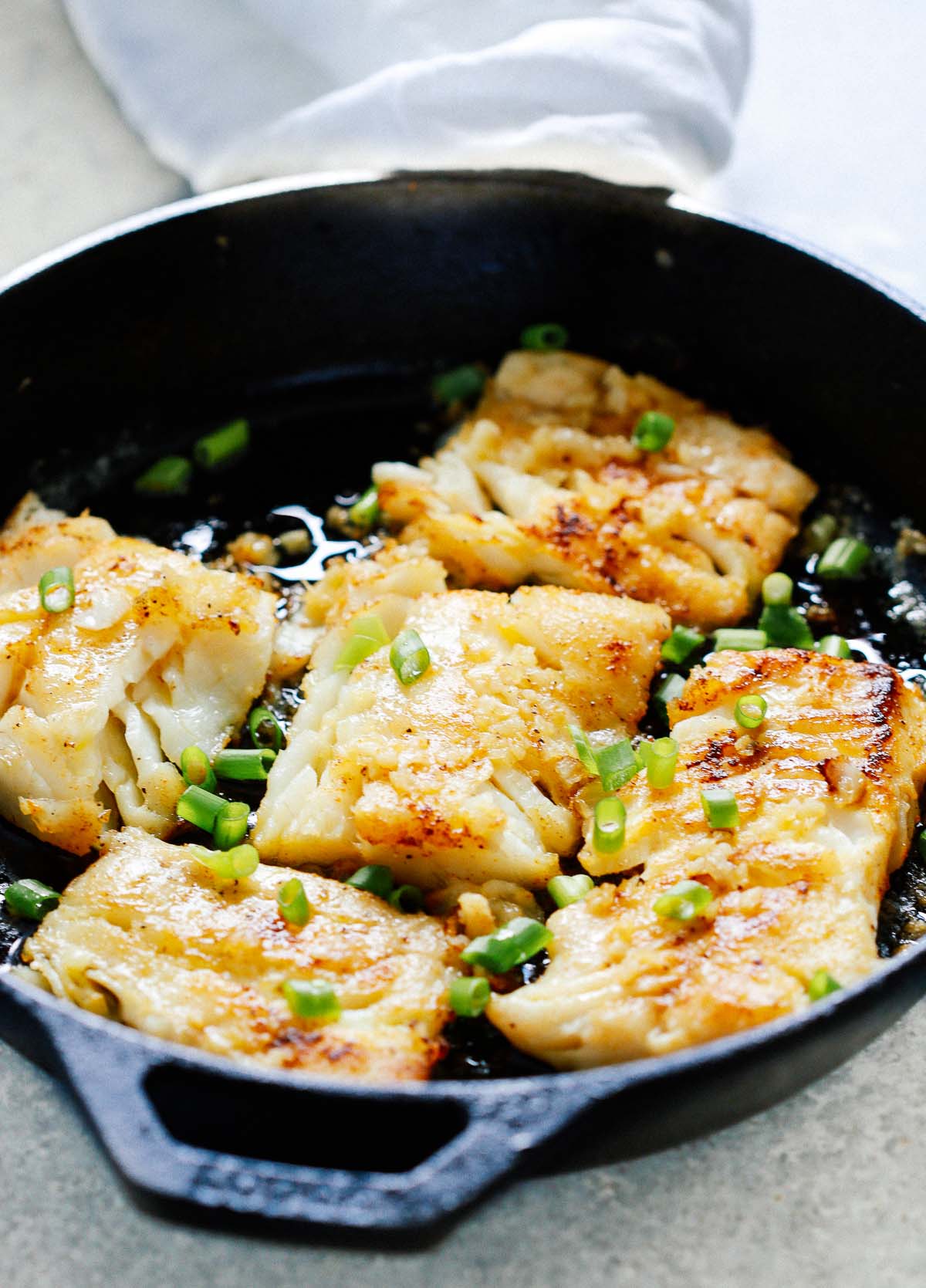 pieces of garlic butter cod cooking in cast iron skillet