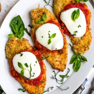 Overhead view of baked chicken parmesan on a white plate
