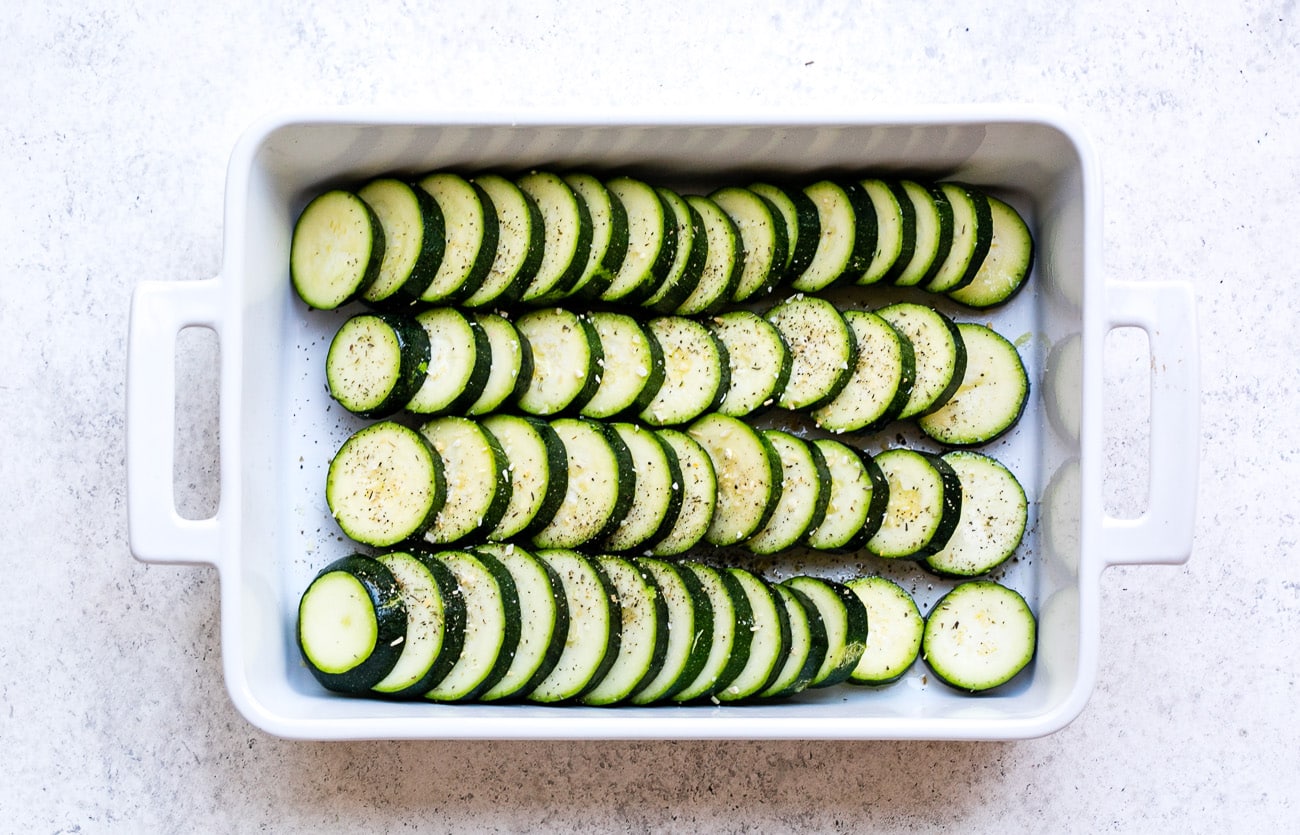Slices of zucchini arranged in baking dish. Slices are seasoned with salt and pepper.