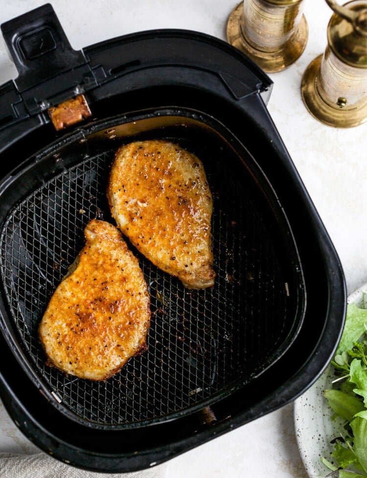 Cooked pork chops in air fryer basket.