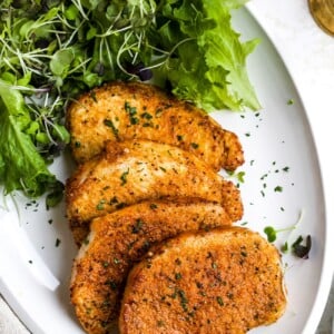 Air fryer pork chops on a white plate with a side salad.