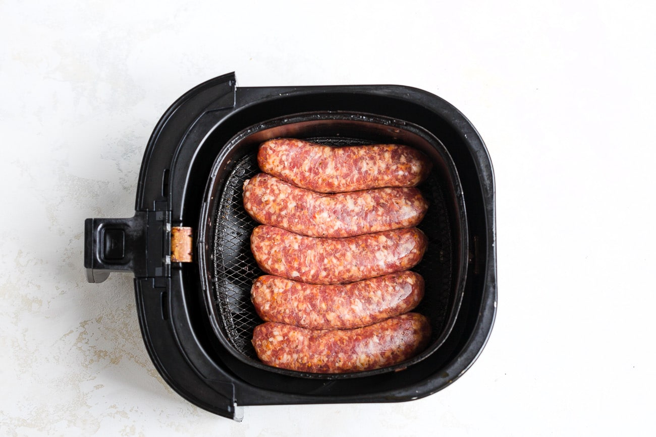 Uncooked sausage in air fryer basket.