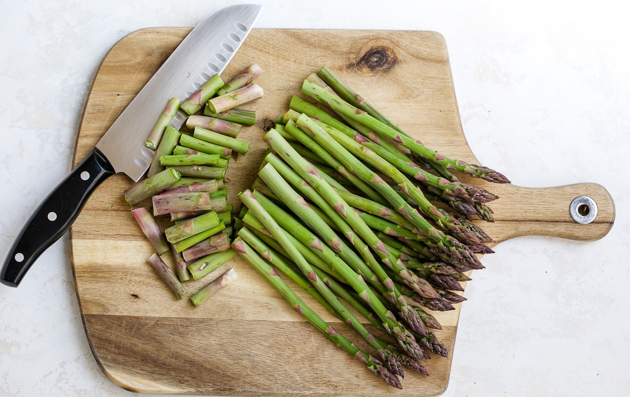 Cutting woody ends from asparagus on cutting board. 
