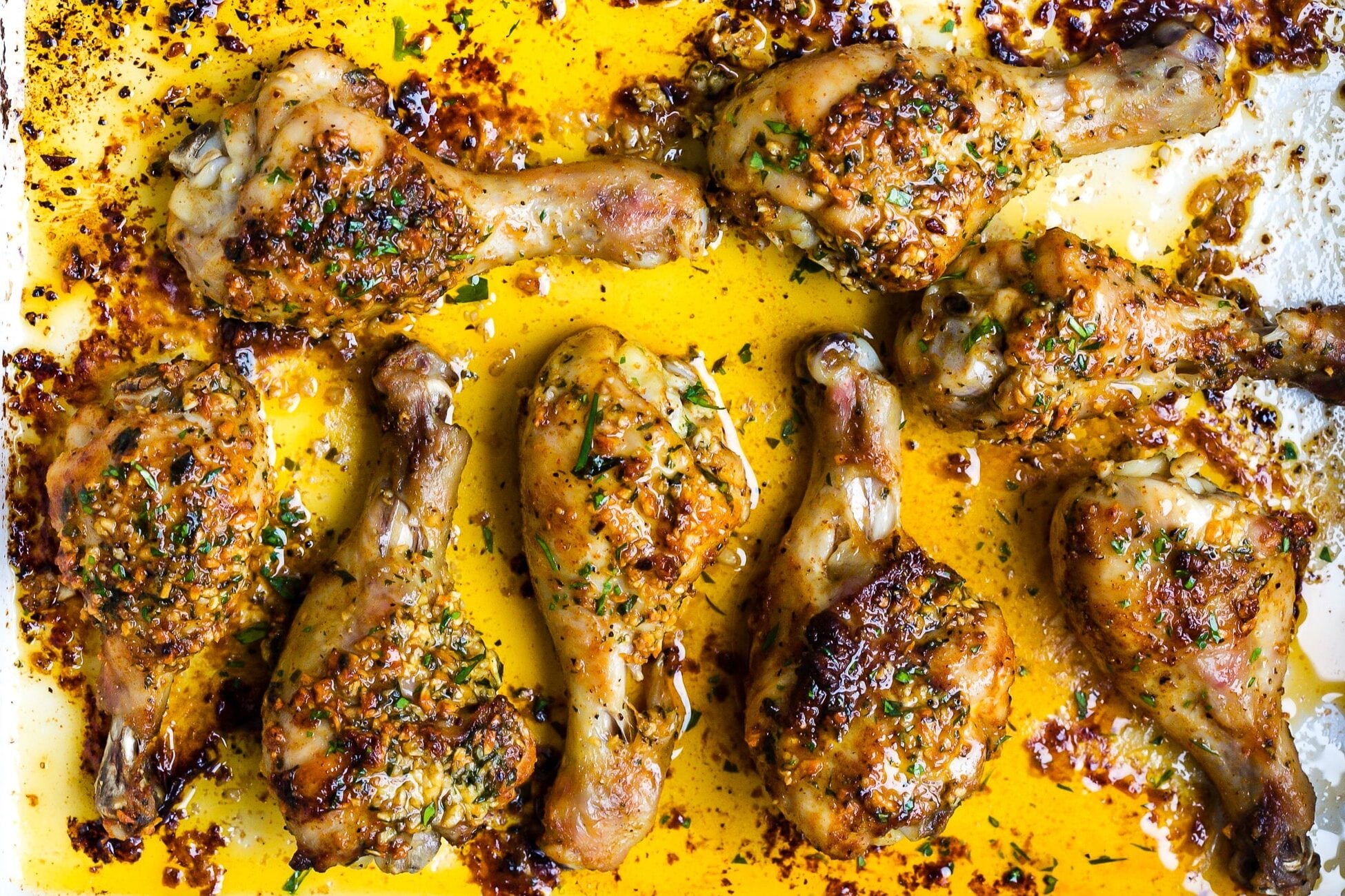 Close up of garlic butter baked chicken drumsticks in a white baking dish.