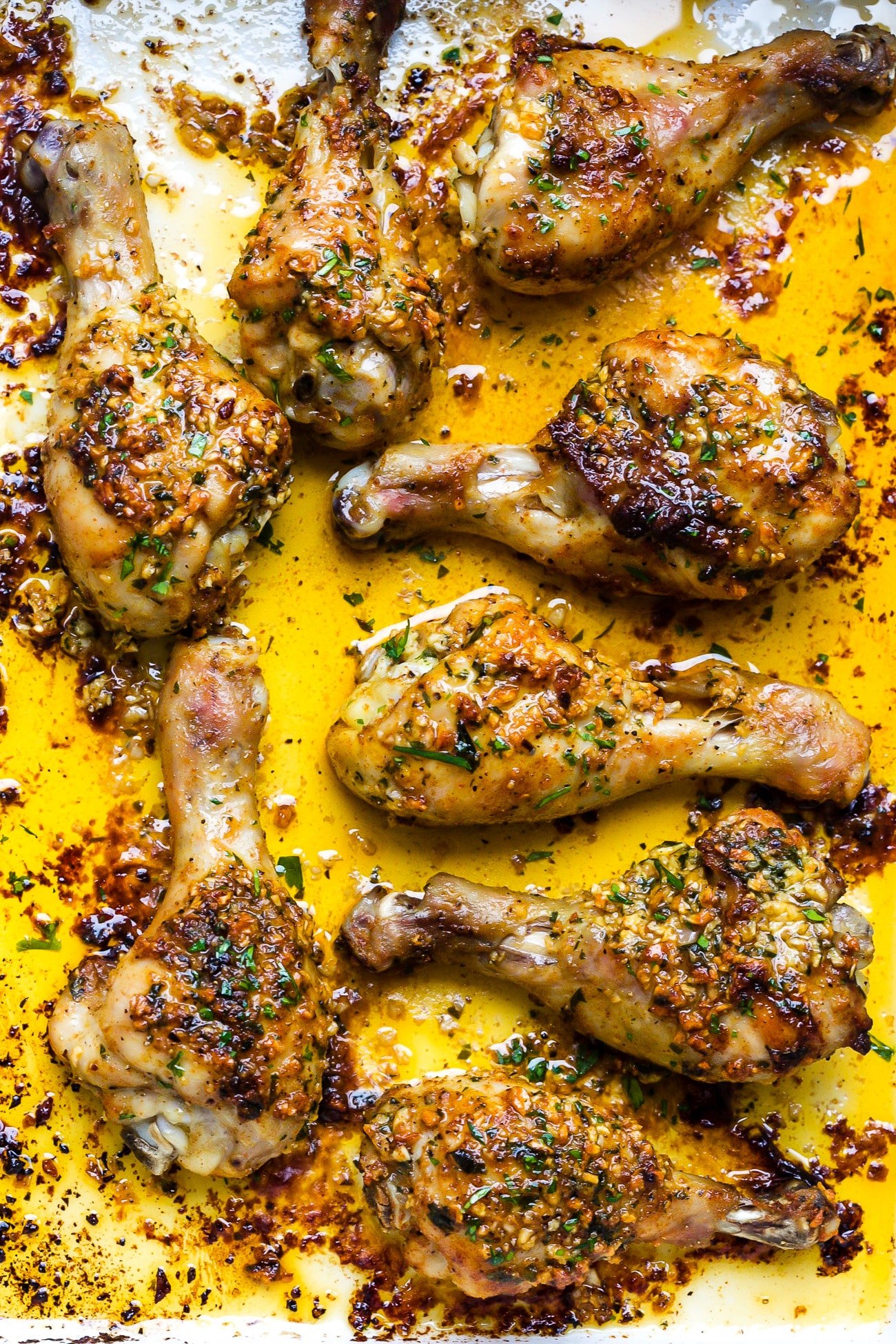 Close up of garlic butter baked chicken drumsticks in a white baking dish. 