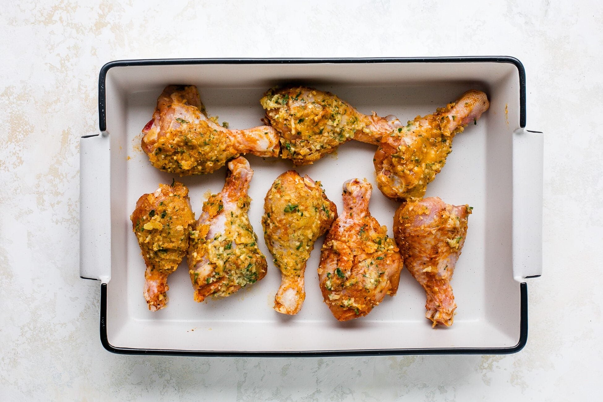 Unbaked, seasoned drumsticks lined in a baking dish.
