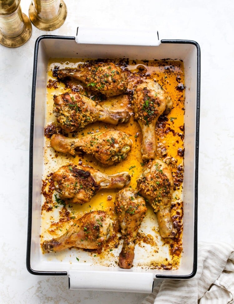 Garlic butter baked chicken drumsticks in a white baking dish.