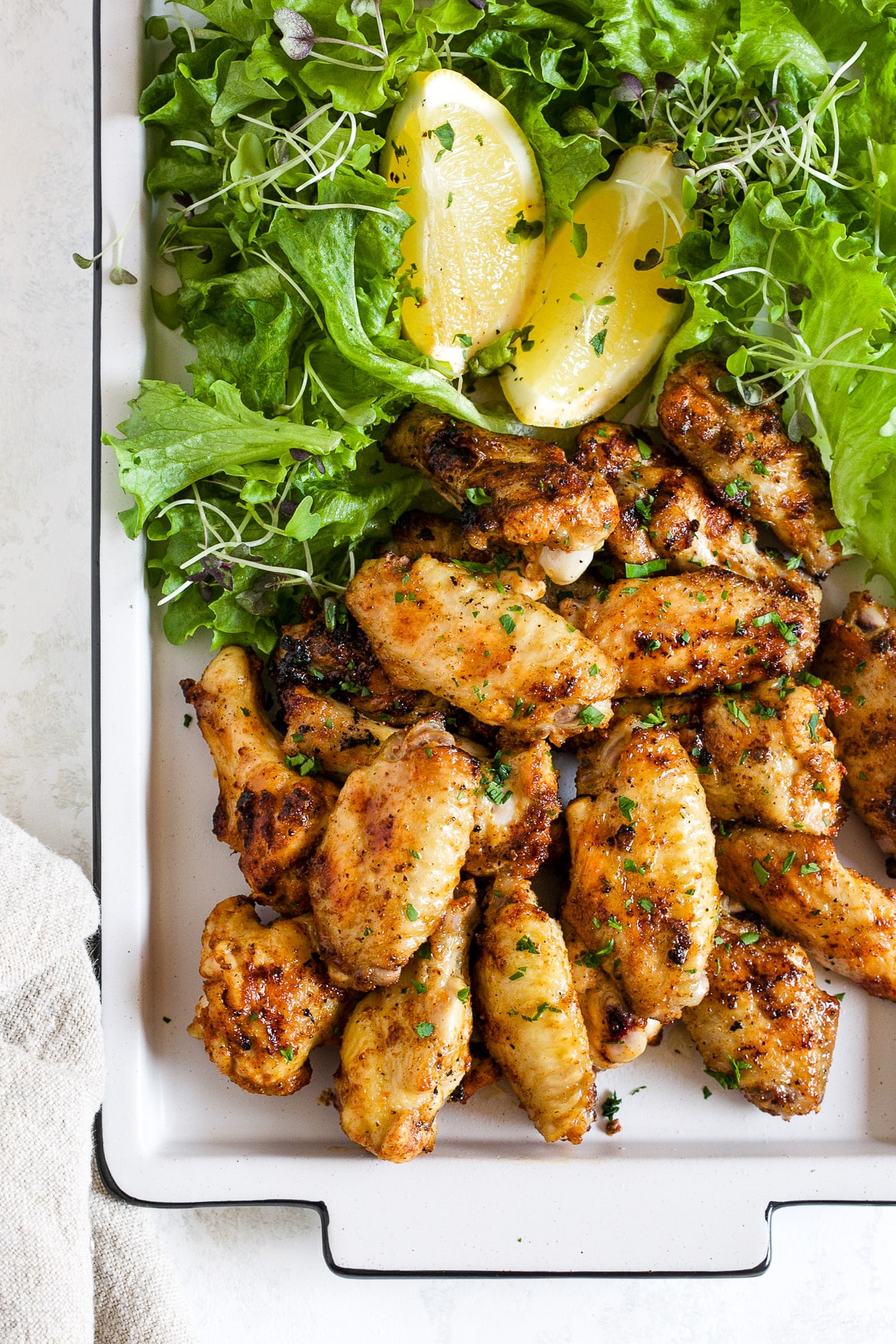 grilled chicken wings on a white platter next to greens and lemon slices