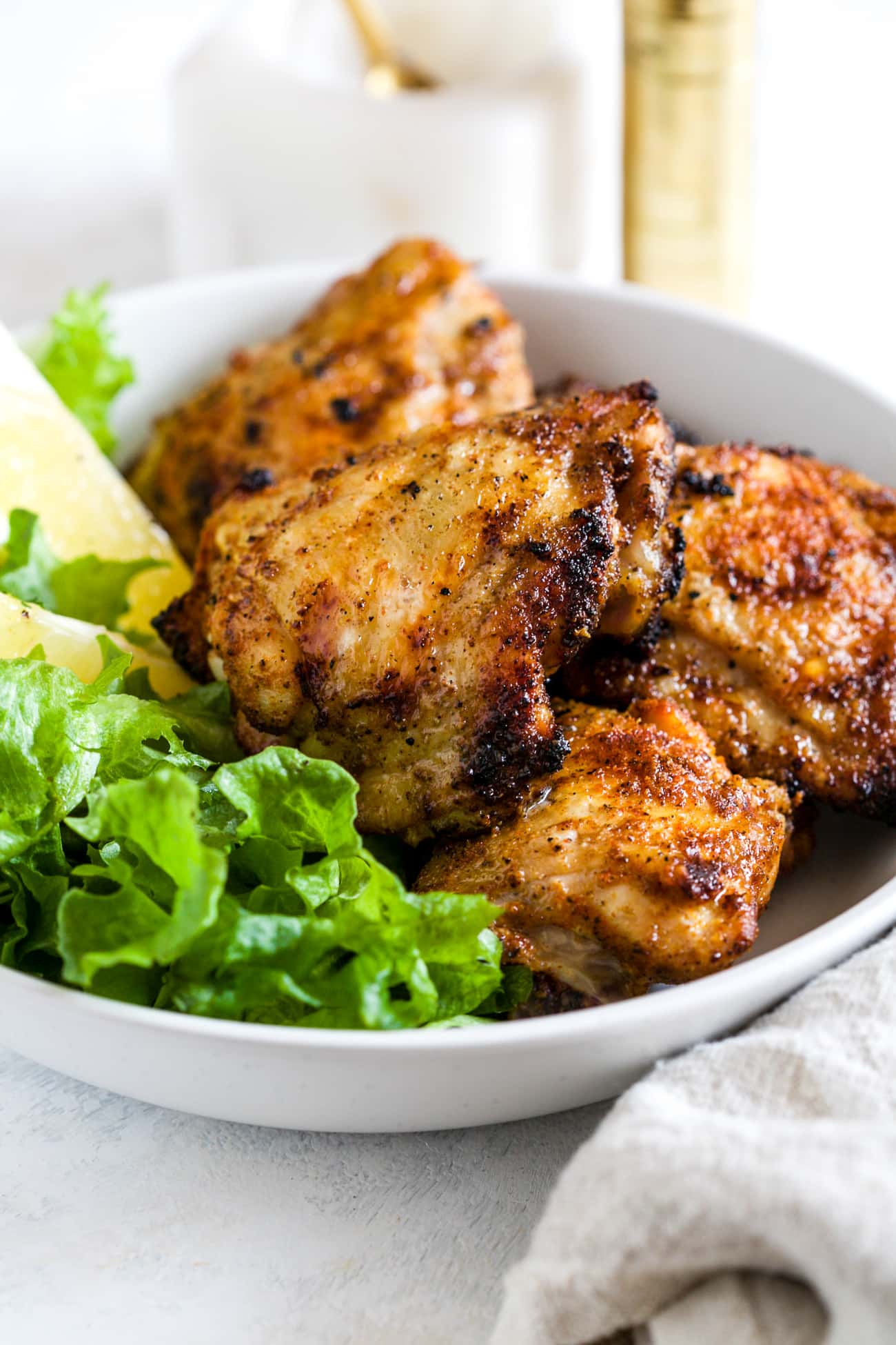 Grilled chicken thighs on a white plate next to lettuce and sliced lemons