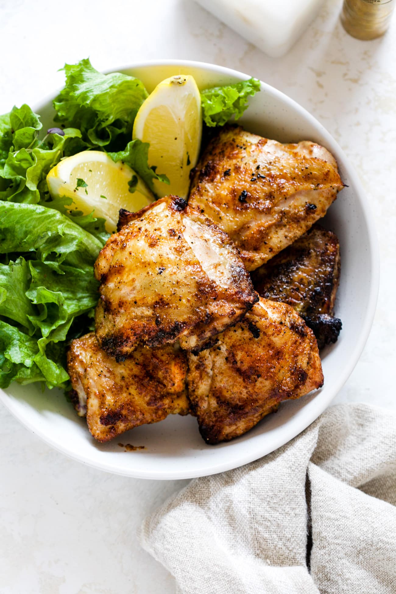 Grilled chicken thighs on a white plate next to lettuce and sliced lemons