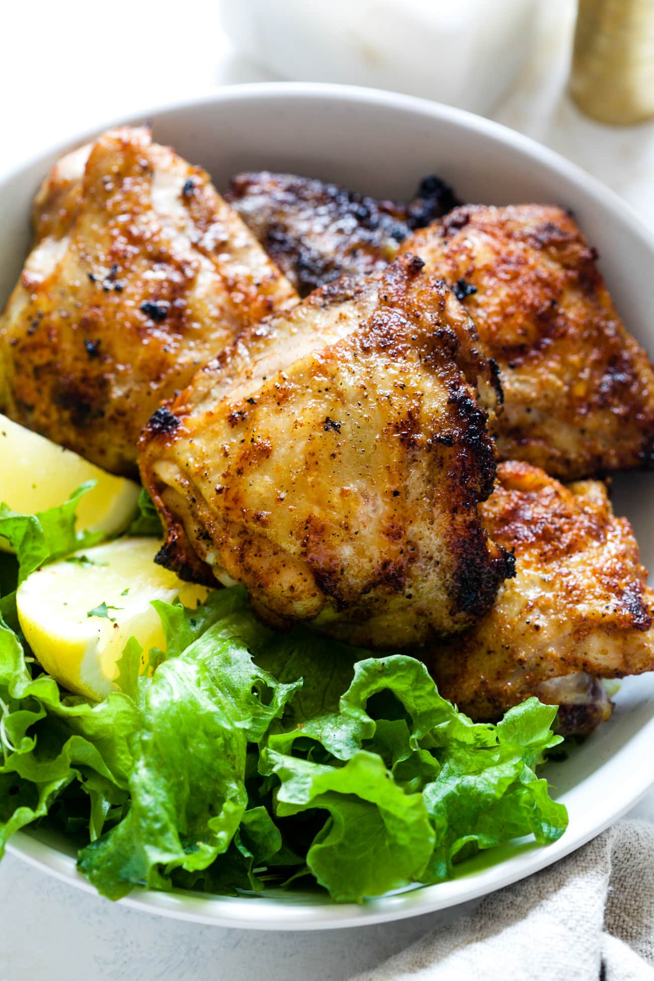 Grilled chicken thighs on a white plate next to lettuce and sliced lemons