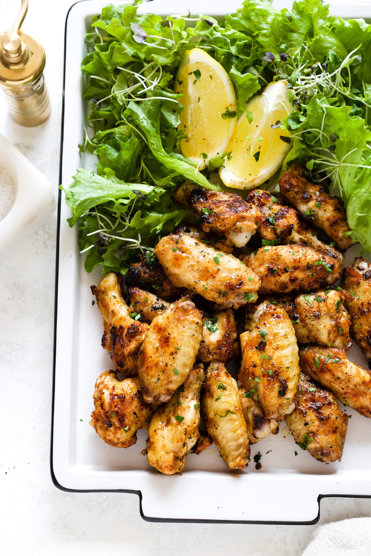 grilled chicken wings on a white platter next to greens and lemon slices