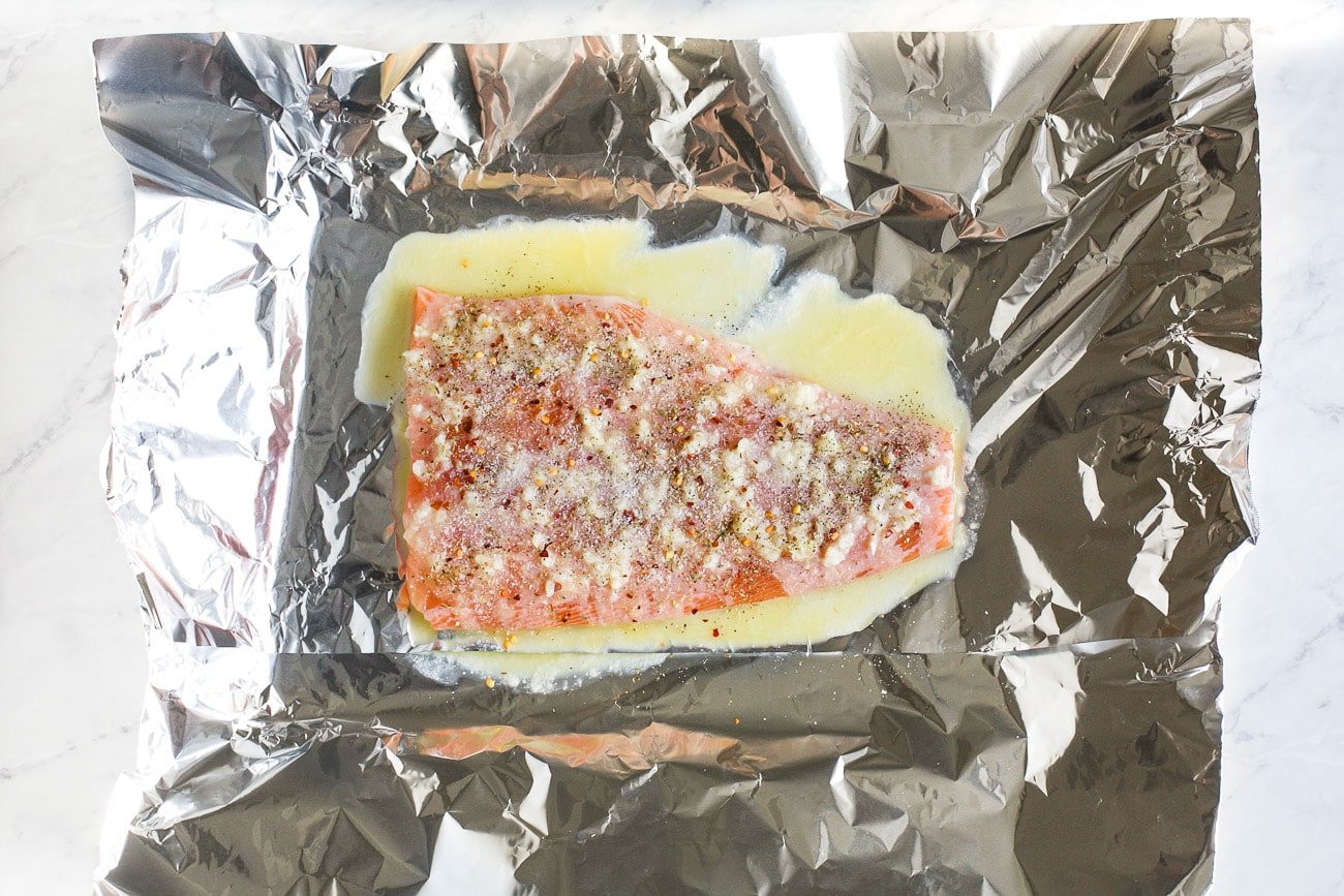 Seasoned and buttered salmon, uncooked, sitting atop a large sheet of foil. 
