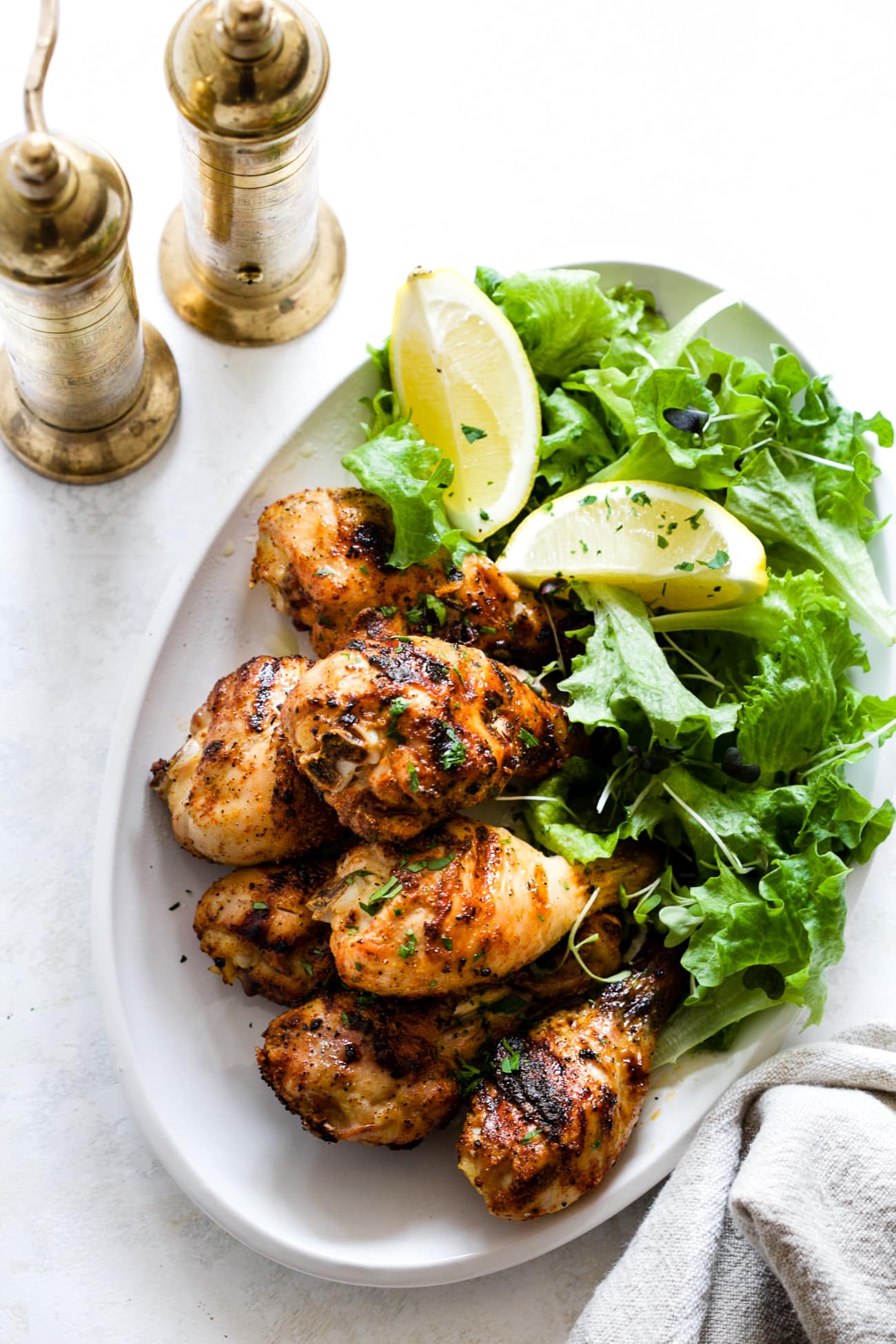 grilled chicken legs with green lettuce and lemon slices on a white plate 