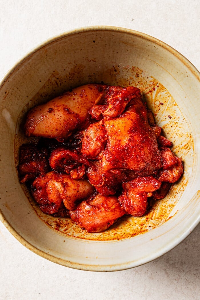 Raw, seasoned chicken thighs in a bowl