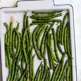 A white baking sheet filled with crispy green beans arranged in neat rows, viewed from above. The image is labeled Crispy Green Beans at the top.