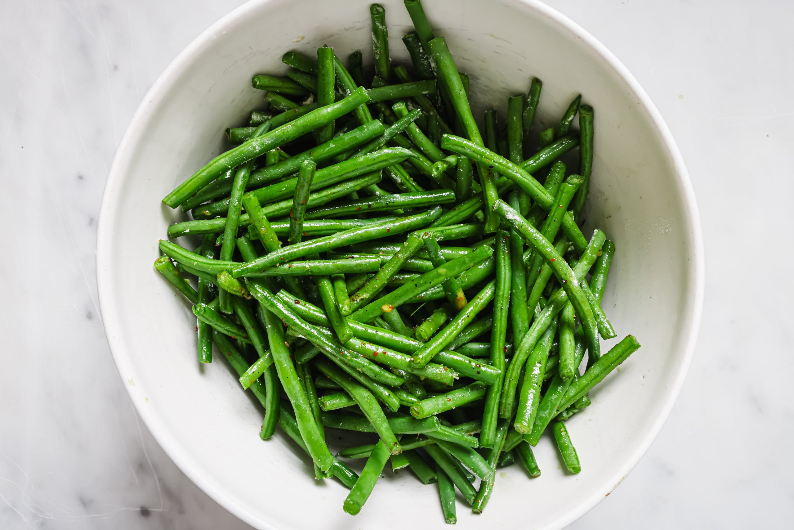 A white bowl filled with fresh, bright roasted green beans on a light marble surface.