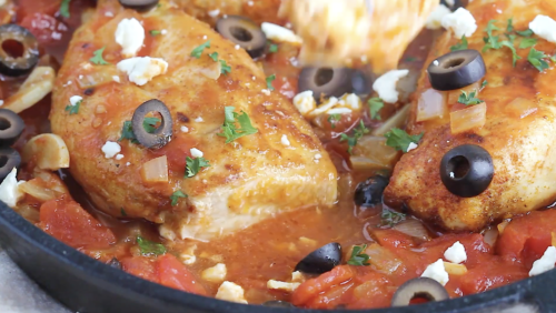 Chicken breasts simmer in a tomato-based sauce with sliced black olives, herbs, onions, and crumbled cheese, garnished with fresh parsley in a skillet for a flavorful Mediterranean Chicken Skillet Recipe.